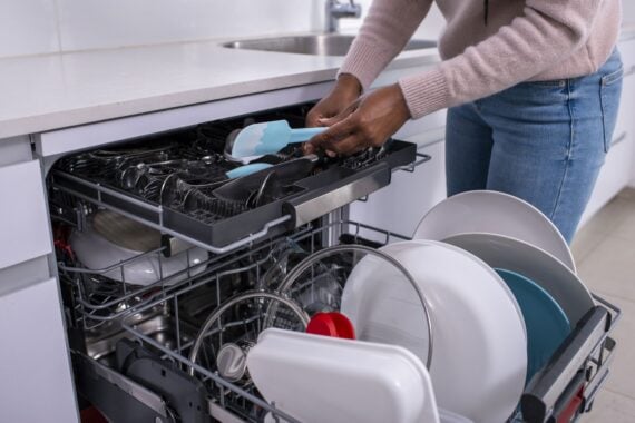 Close up image of a woman's hands holding a spatula, taking out clean cutlery from the dishwasher rack.
