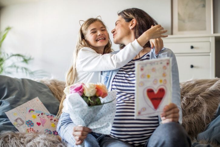 Daughter surprising pregnant mother on Mother's day, with bouquet and greeting card