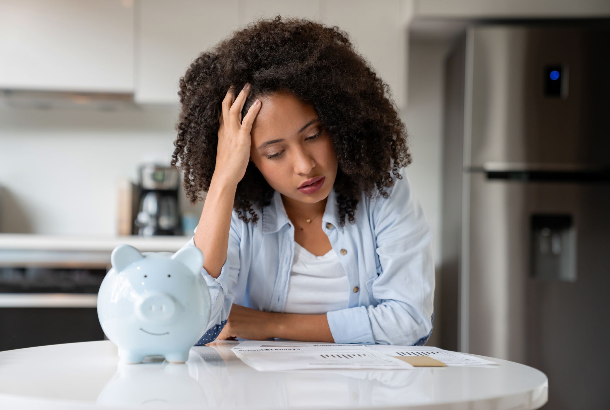 Woman looking worried about having to pay her bills and using her savings from a piggybank - home finances concepts