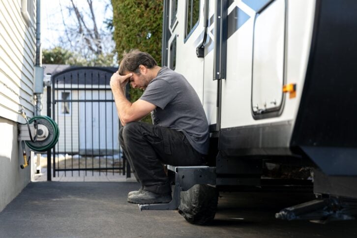 Man crying or being depressed after vacations are cancelled due to Covid-19 pandemic crisis. The woman is sitting on the steps of the travel trailer and feeling depressed.