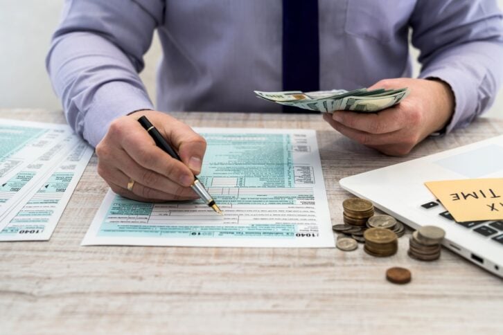 businessman counts dollars and fills out a US 1040 individual tax form. Sticker with the inscription tax time. Tax concept.