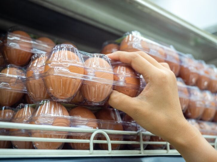 Close-up hand picking raw of eggs in a plastic egg tray from shelf in store. Fresh egg in clear plastic egg box.