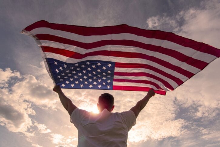 Man holding waving American USA flag in hands during warm sunny evening in USA, concept picture