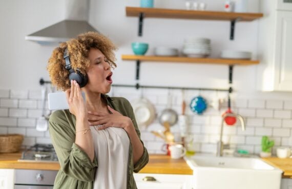 Very happy African American woman having fun listening to music at home and dancing in the kitchen.