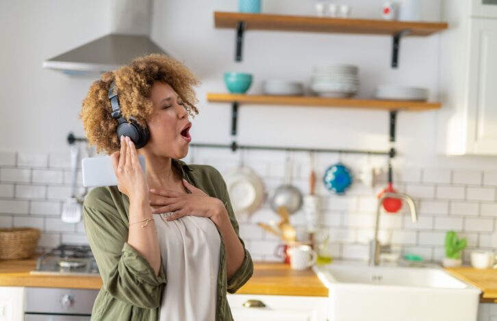 Very happy African American woman having fun listening to music at home and dancing in the kitchen.
