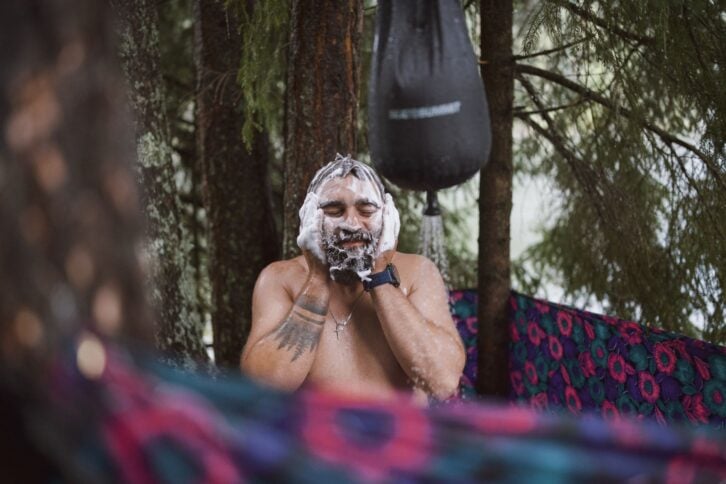 Adult male is taking a bath at the nature with a water bag outdoor shower