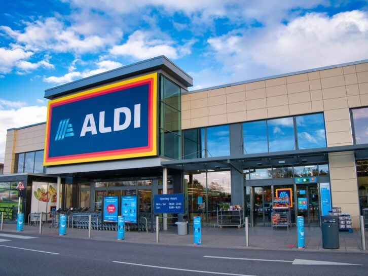 The Aldi logo is displayed on the front of one of its stores in a local retail park on Wirral, U.K., on a sunny afternoon.