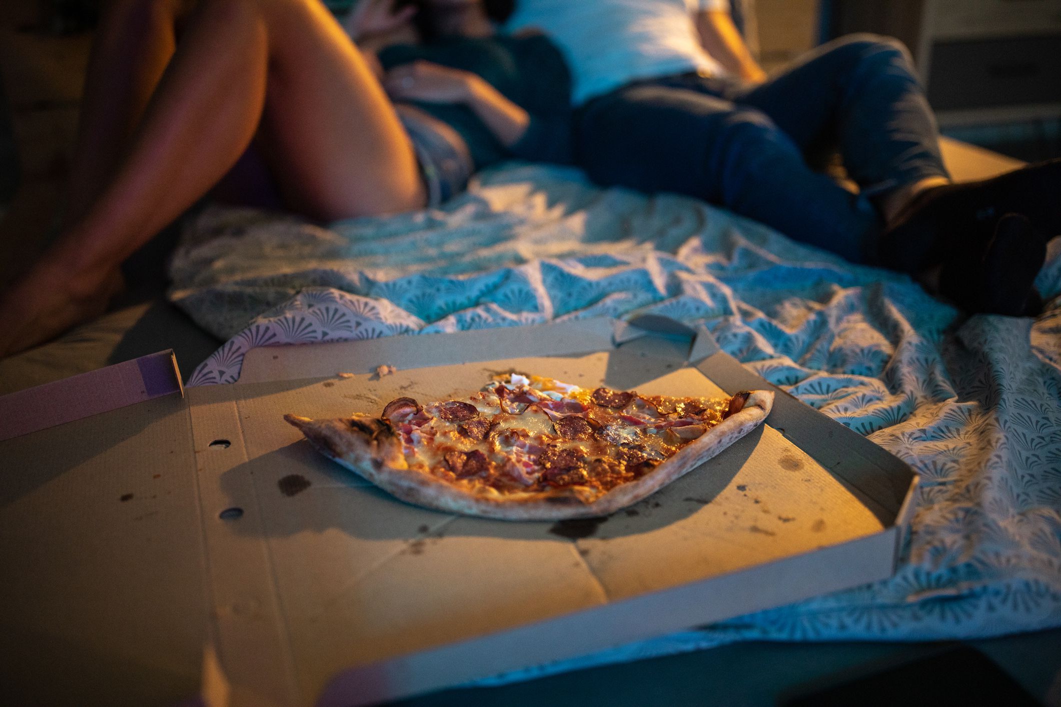 Happy couple watching tv and enjoying pizza in bedroom at night