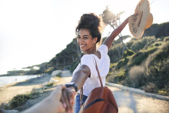 Young woman enjoying her vacation at the sea -Woman walking on a path by the beach, holding a friend's hand - Concept of freedom enjoyment