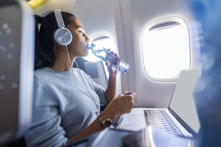 Close up of young beautiful business woman drinks water on a plane