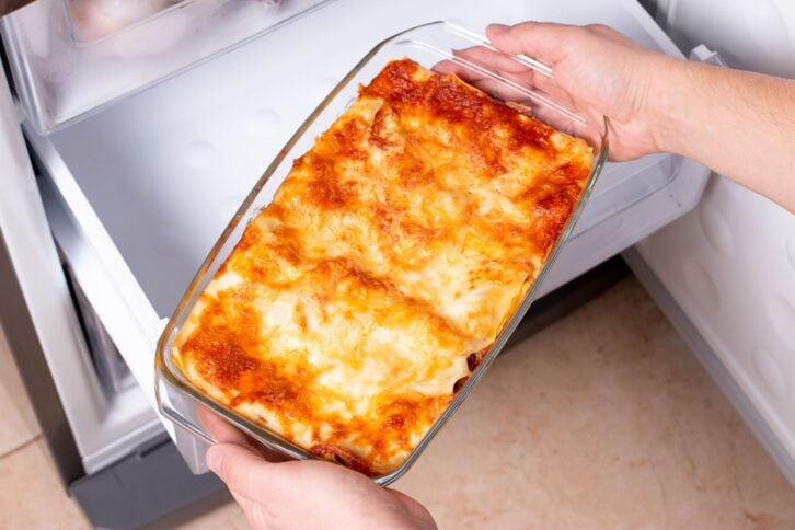 Frozen food. Man's hands are taking frozen lasagna from the freezer of the fridge. Concept of ready made frozen dishes and saving time on cooking food.