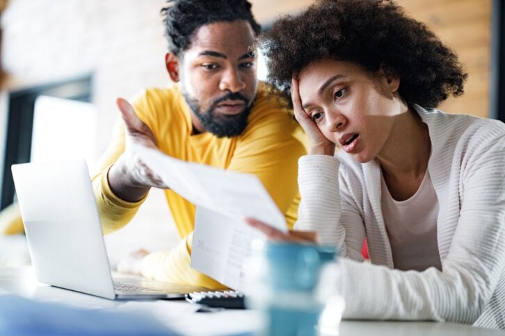 Young African American couple feeling frustrated while paying their bills over laptop at home. Focus is on woman.