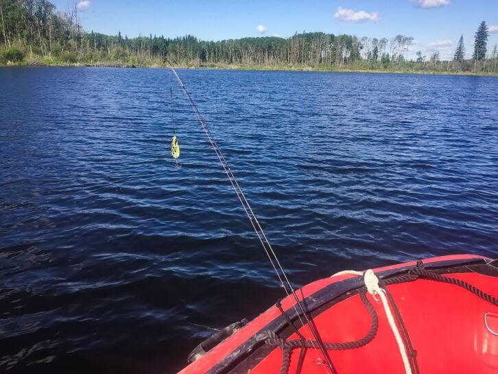 A fishing rod with hook over the edge of a boat in water.