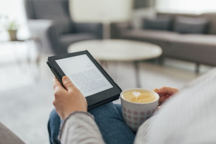 Woman sitting on sofa and reading e-book at home.