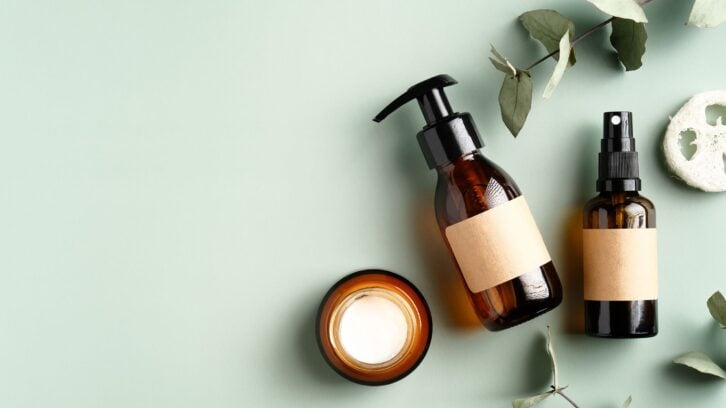 Natural organic SPA cosmetic products set with eucalyptus leaves. Top view herbal skincare beauty products on green background. Amber glass dispenser, spray bottles, jar of moisturizer cream.