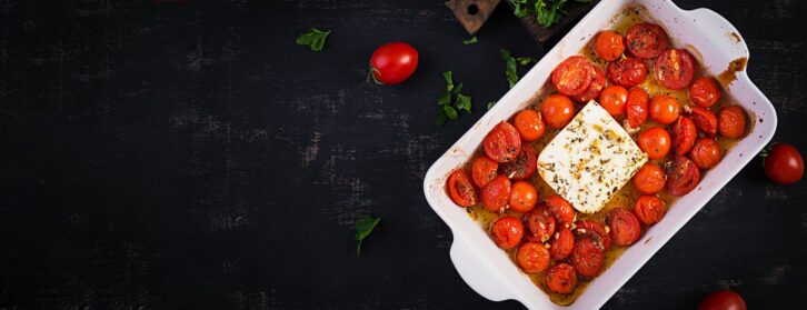 Fetapasta. Trending viral Feta bake pasta recipe made of cherry tomatoes, feta cheese, garlic and herbs in a casserole dish. Top view, banner, copy space.