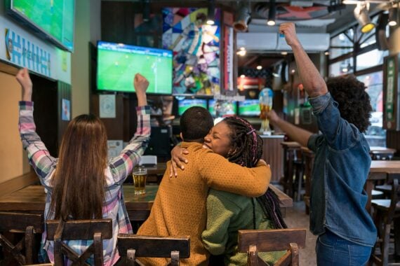 Back view of diverse friends celebrating Argentina's triumph on a football match at the bar hugging while enjoying beer