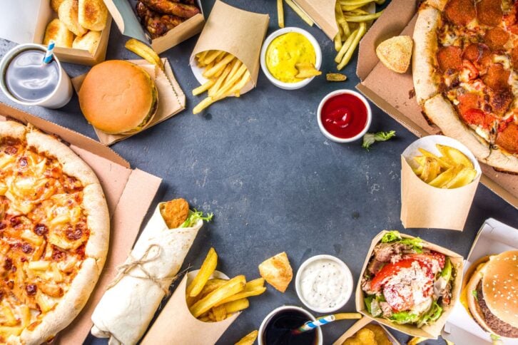 Delivery fastfood ordering food online concept. Large set of assorted take out foods pizza, french fries, fried chicken nuggets, burgers, salads, chicken wings, sides, black concrete background