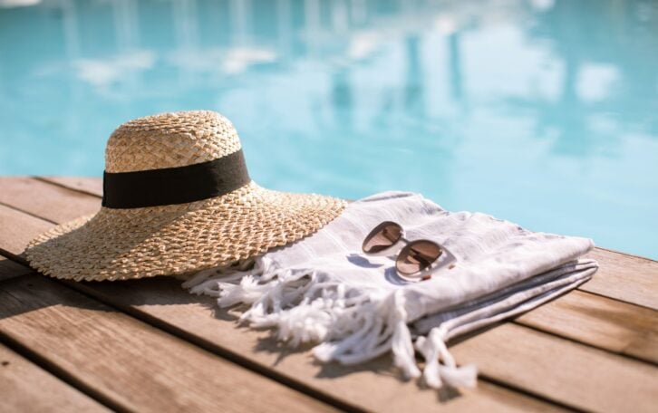 Sunglasses and straw hat on the wooden floor at the pool. Summer Vacation Fashion Concept.