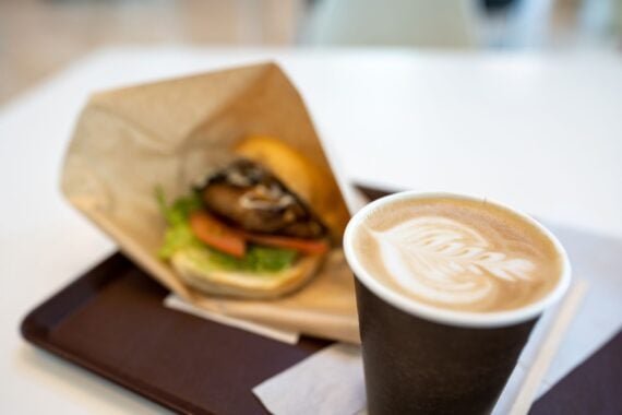Cappuccino with latte art and fresh burger blurred in the background on a tray