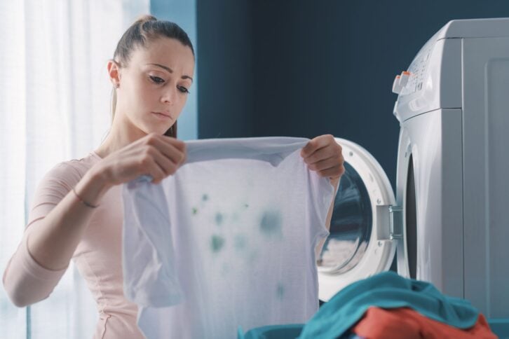 Disappointed woman standing next to the washing machine and holding stained clothes