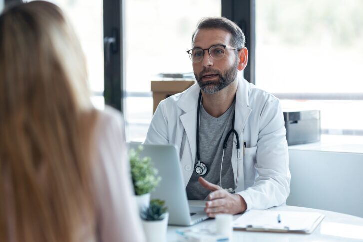 Shot of handsome mature male doctor talking while explaining medical treatment to patient in the consultation.