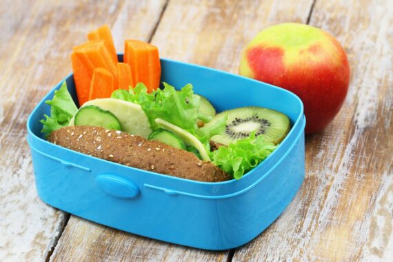 Healthy school lunch consisting of brown cheese roll, fresh carrots and kiwi fruit and apple