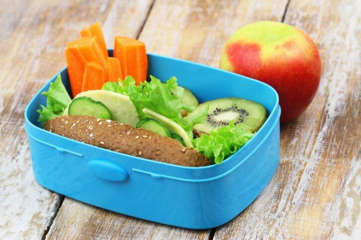 Healthy school lunch consisting of brown cheese roll, fresh carrots and kiwi fruit and apple