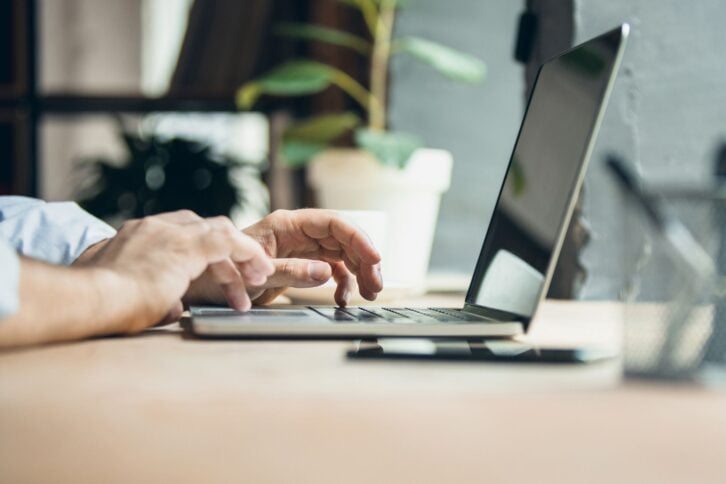 Arms on keyboard. Side view. Cropped image of male hands in front of laptop screen typing text or message. Concept of communication, interaction, modern technologies