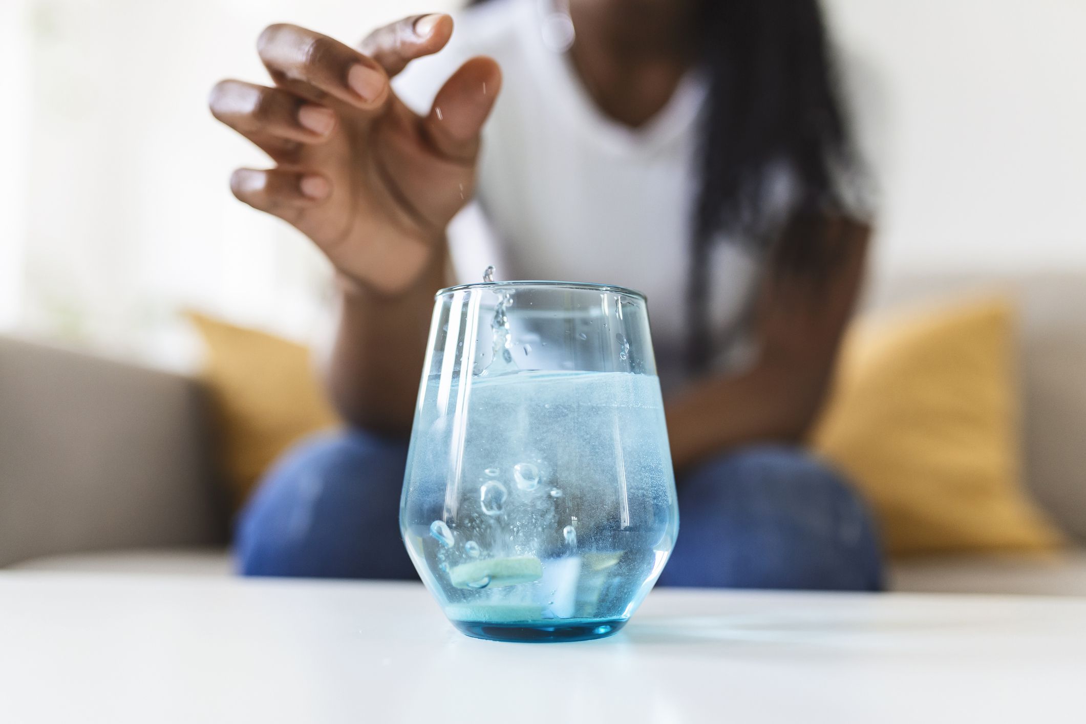 Closeup of a young woman dropping an effervescent antacid in a glass of water. young woman hardly put a soluble pill with a medicine for pain or a hangover in a glass of water