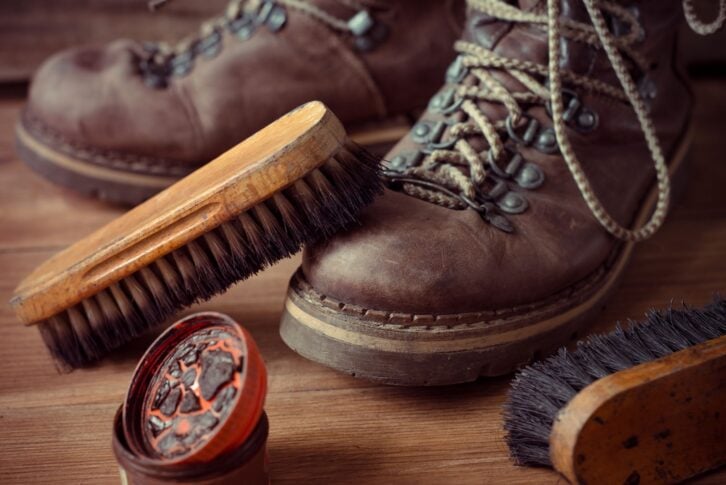 Old vintage leather boots with shoe brush on wooden background
