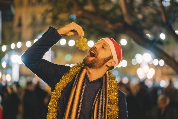 Happy man celebrating New Year in Valencia and eating grape outside at night