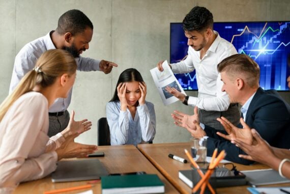 Conflicts At Work. Unhappy Asian Female Employee Suffering From Mobbing And Bullying In Office, Upset Employee Lady Covering Ears While Aggressive Coworkers Shouting At Her During Corporate Meeting