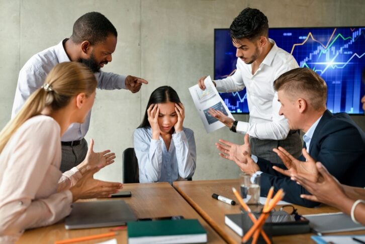 Conflicts At Work. Unhappy Asian Female Employee Suffering From Mobbing And Bullying In Office, Upset Employee Lady Covering Ears While Aggressive Coworkers Shouting At Her During Corporate Meeting