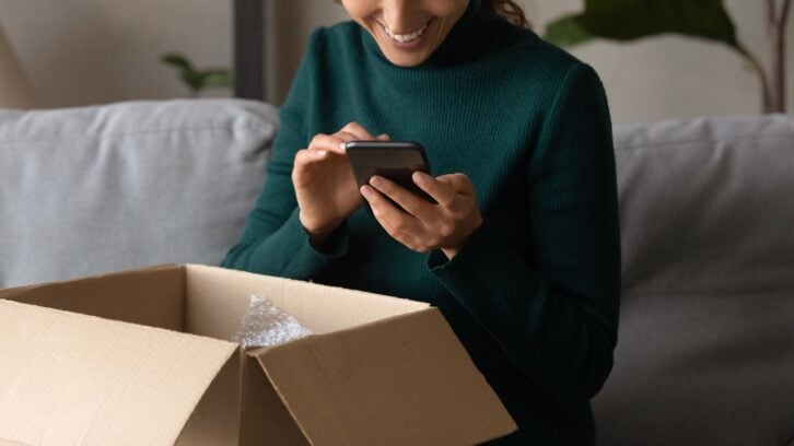Positive feedback. Close up of young woman leaving comment at web store site after receiving parcel with goods purchased. Smiling millennial female order consumer products delivery online using phone