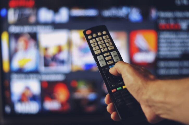 Male hand holding tv remote control. The focus of the photo is on the remote control. The background and hand are blurred