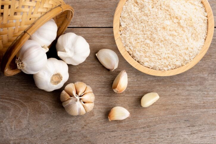 Garlic powder in wooden bowl and bulb of garlic isolated on wooden table background. Top view. Flat lay.