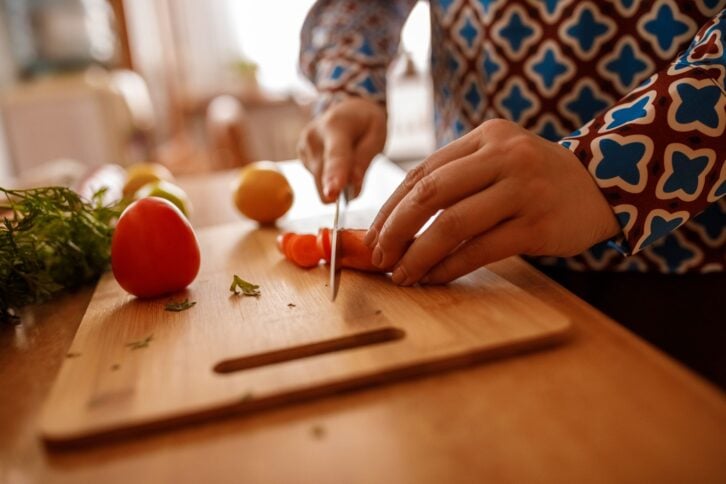 Close up shot of unrecognizable woman standing over a kitchen counter and chopping a carrot for a delicious meal she is preparing.
