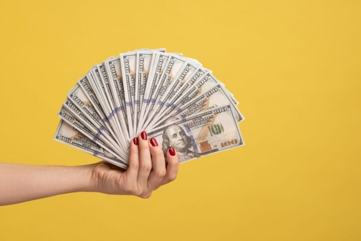 Side view closeup of woman hand showing fan of dollar banknotes, arm holding cash, lot of money and wealthy life, big profit, financial income. Indoor studio shot isolated on yellow background.