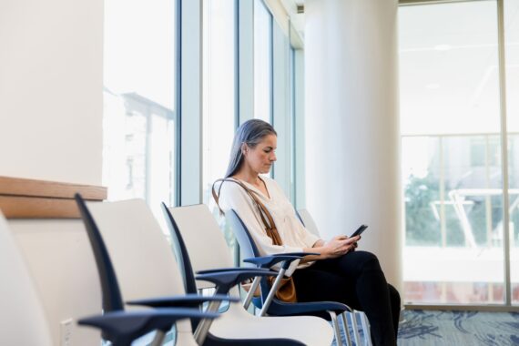 The mid adult woman uses her smart phone as she sits in the hospital waiting room.
