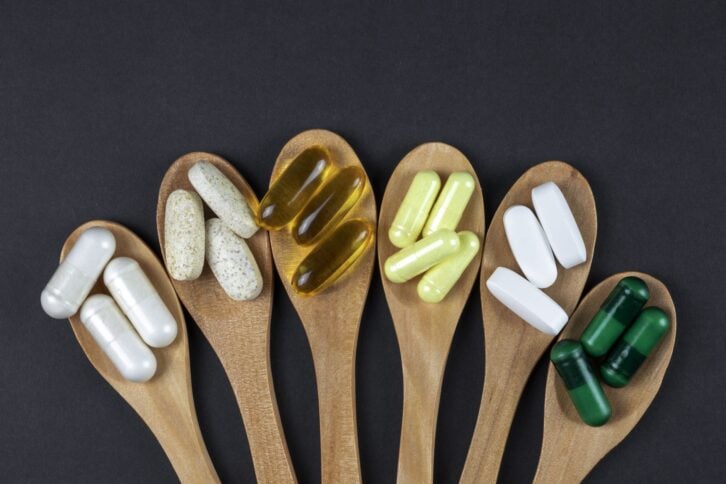 Healthy vitamins and supplements on wooden teaspoons against dark black background with copy space.