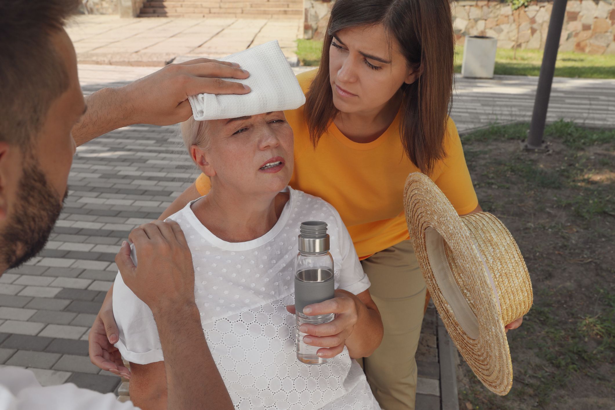 People helping mature woman on city street. Suffering from heat stroke