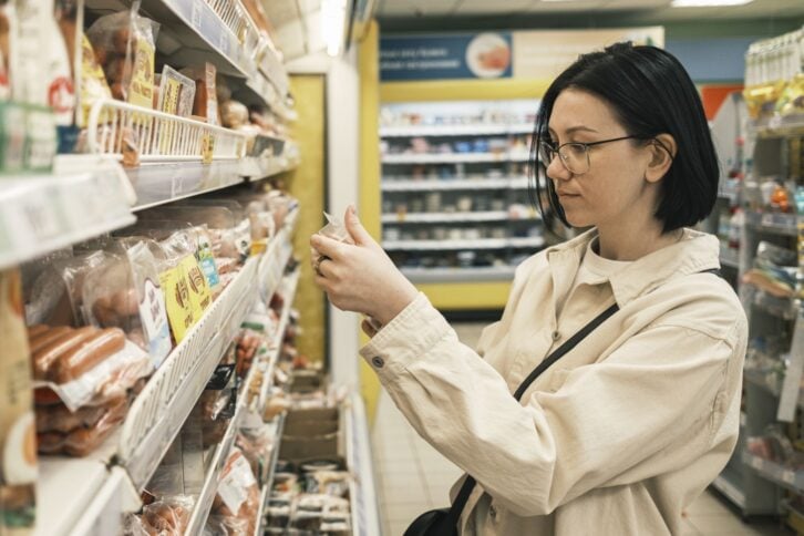 A young woman in a grocery supermarket chooses food and carefully reads the composition of the products. Shopping concept