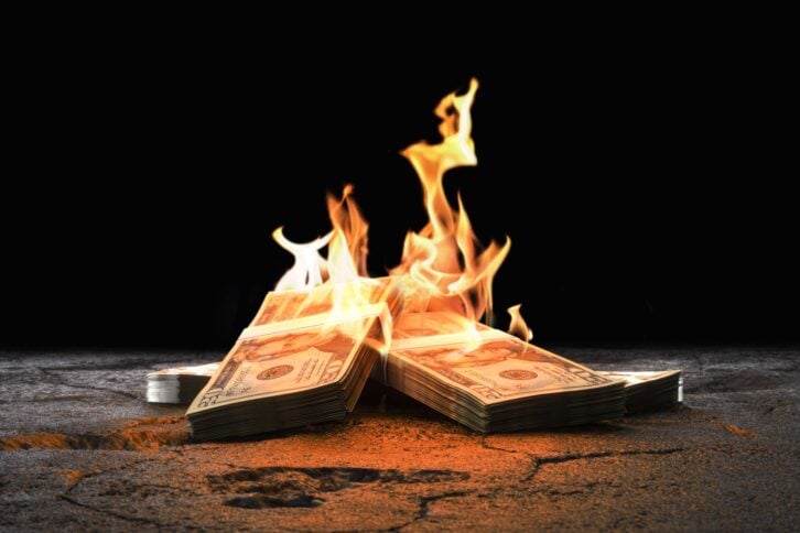 Closeup heap of Dollar bills burning with orange fire on rough cracked ground against black background as symbol of inflation economic collapse. 3d render