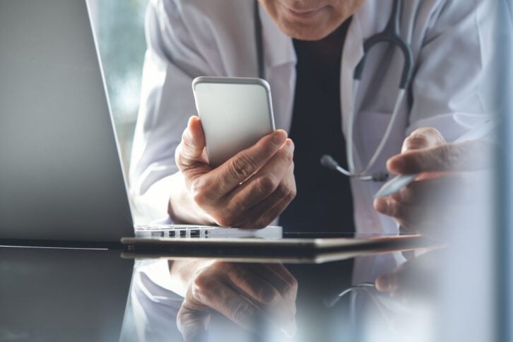 Close up, doctor using mobile smart phone, working on laptop computer during the conference with stethoscope on desk, digital data, medical electronic record system, medical technology background