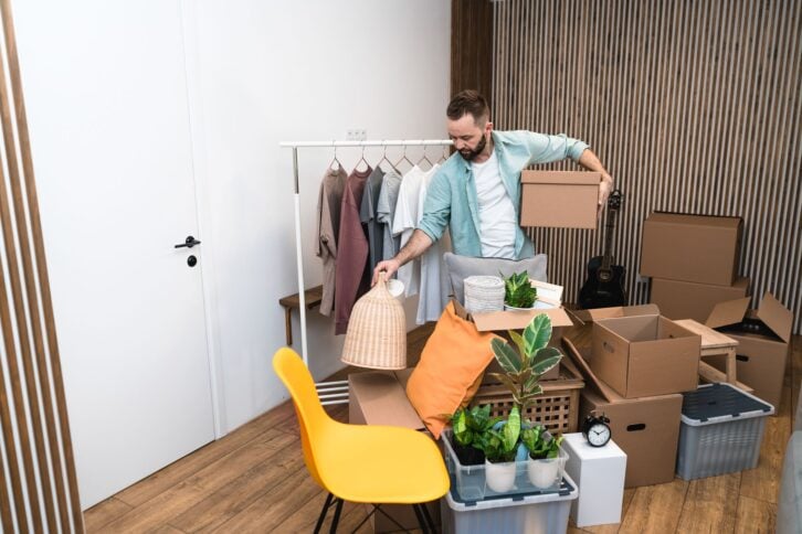 Mature man unpacking things from boxes while moving in new unfurnished apartment.