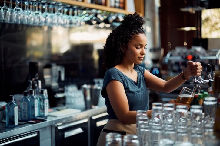African American female barista pouring beer from a beer tap while working in pub.