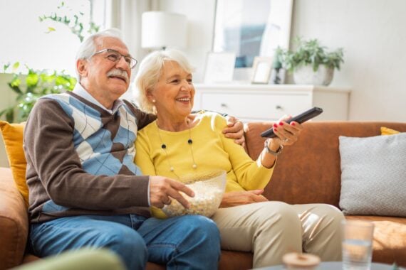 Senior couple at home, spending relaxed day together. They are watching TV or reading book.