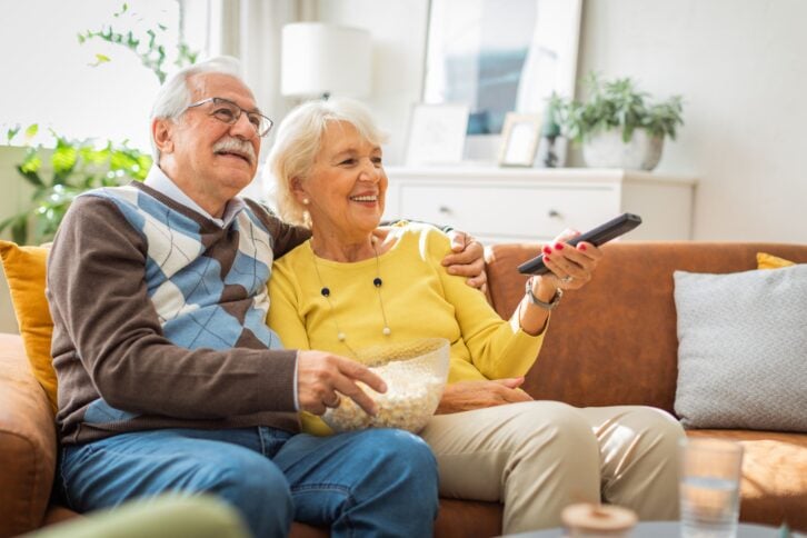 Senior couple at home, spending relaxed day together. They are watching TV or reading book.