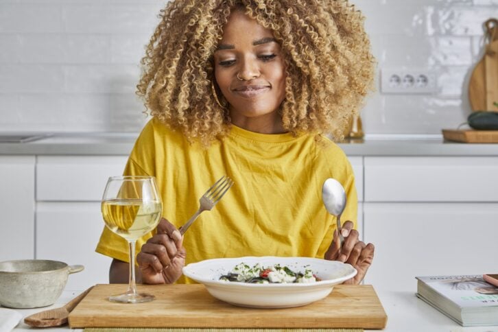 A beautiful multiracial young adult woman in the kitchen, looking at the meal she had prepared with satisfaction, representing healthy lifestyle, wide angle image